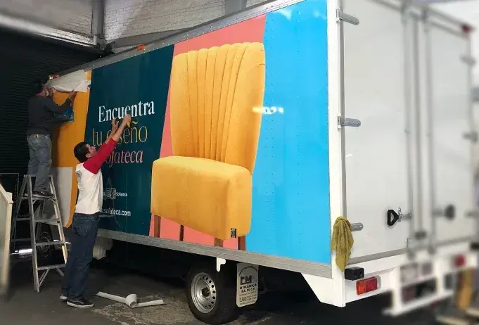 Dos personas aplican una gráfica adhesiva de colores al lateral de un camión